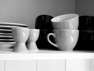 Verschiedene Tassen, Teller und Eierbecher in einem Schrank schwarzweiß
