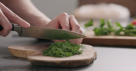 man chopping fresh dill on olive board side view