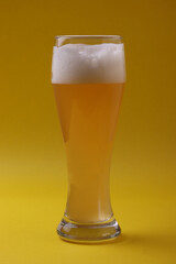 pub weise beer made of wheat with white foam in a glass  on the yellow background