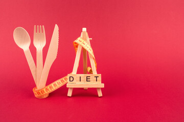 Diet concept - wooden cutlery, yellow measuring tape and word DIET on wooden bricks, on red burgundy background with copyspace. Healthy and sustainable lifestyle