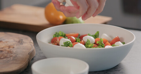 man add mozzarella into salad with kale and tomatoes in white bowl on kitchen countertop