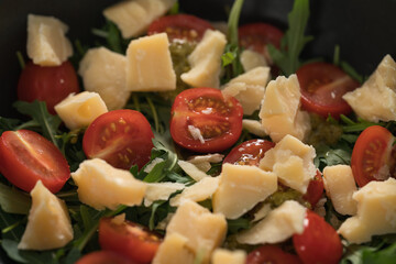 Fresh salad with cherry tomatoes, arugula and hard vintage cheese in black bowl closeup