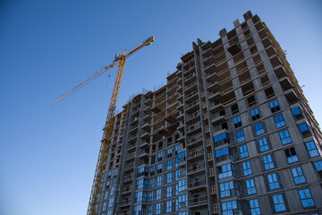 Tower crane working at construction site on blue sky background with white clouds. Construction process of the new residential buildings. Installing double glazed windows