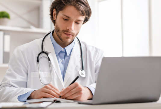 Doctor Watching Webinar On Laptop And Taking Notes