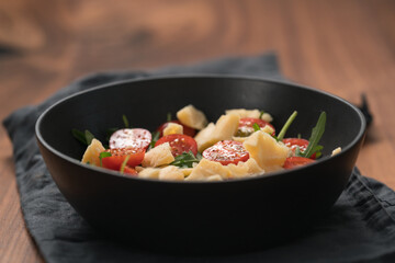 Fresh salad with cherry tomatoes, arugula and hard vintage cheese in black bowl on linen napkin