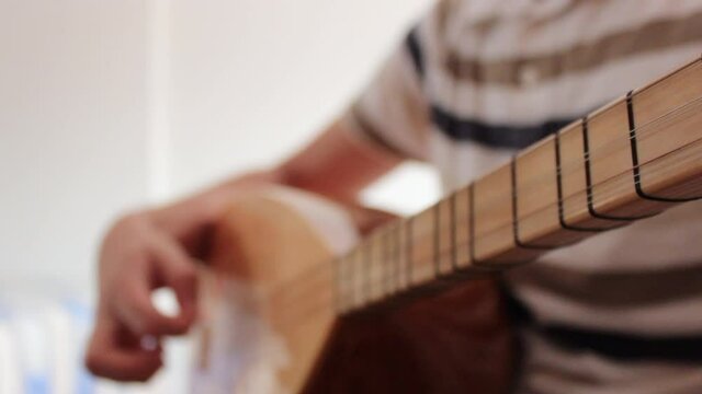 Young man is playing saz baglama. Baglama is traditional Turkish music instrument.