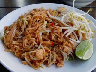 Chicken pad thai dish served on a white plate, with a slice of lime