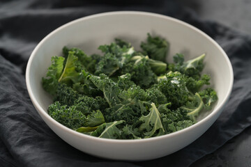 kale salad leaves in white bowl on linen napkin with other ingredients on background