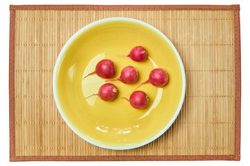 five red radishes on a yellow plate on a cane place mat