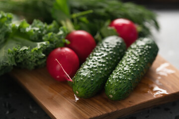 Radish, cucumbers and kale leaves on olive wood board closeup