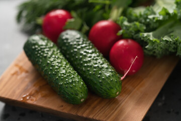 Radish, cucumbers and kale leaves on olive wood board closeup
