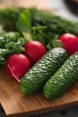 Radish, cucumbers and kale leaves on olive wood board closeup