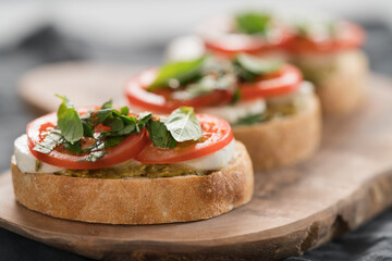 Bruschetta with mozzarella, tomatoes and basil with pesto on olive wood board