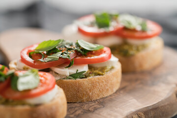 Bruschetta with mozzarella, tomatoes and basil with pesto on olive wood board