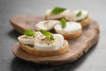 Bruschetta with mozzarella, basil and pesto on olive wood board