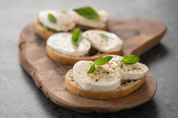 Bruschetta with mozzarella, basil and pesto on olive wood board