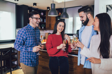 Young people cheering with champagne flutes and looking happy while having home party.