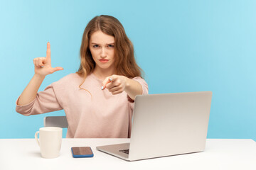 You are fired! Angry woman boss sitting at workplace and showing loser gesture, pointing to camera,...