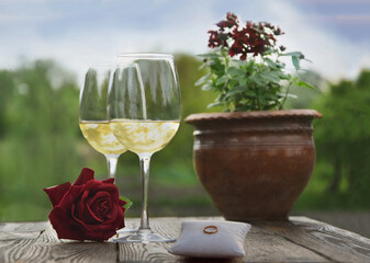 Wedding ring, glasses with wine, rose, on a background of nature.