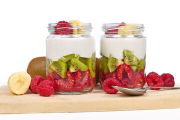 Two glasses of healthy layered snack with raw raspberry and kiwi fruits and yoghurt on white background