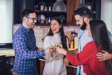 Young people cheering with champagne flutes and looking happy while having home party.