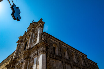 Fototapeta na wymiar Amazing church of St. Maria, Mesagne, Puglia, Italy. Portrait mode view, clear blue sky, hot summer day, travel photography, taken from across the streets under pharmacy store cross sign