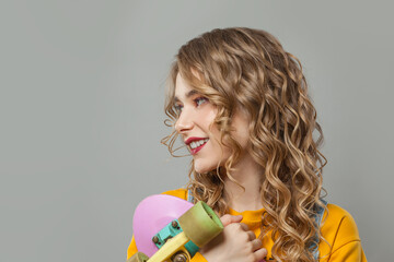 Young woman holding skateboard on gray background