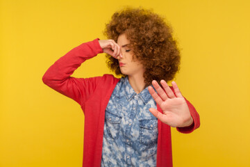 Awful odor! Portrait of confused woman with curly hair pinching nose to avoid bad smell and showing...