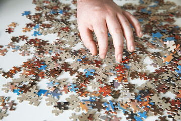 Male hand reaching for jigsaw puzzle piece.