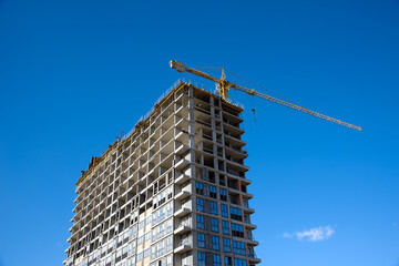 Fototapeta premium Tower crane working at construction site on blue sky background with white clouds. Construction process of the new residential buildings. Installing double glazed windows