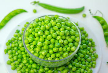 Close up fresh green peas in a glass bowl and pods on a white background