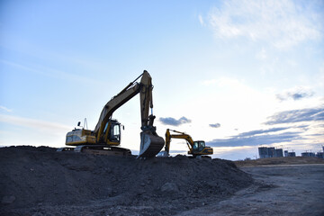 Excavators work at constrruction site on sunset background. Backhoe digs gravel and old concrete....