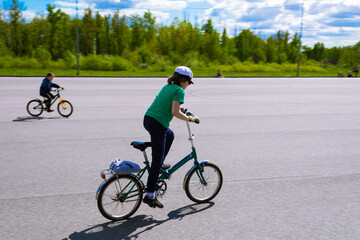 Fototapeta na wymiar Boy riding a bicycle on the asphalt on a background of green trees. Soft focus, blur.