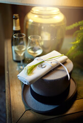Elegant wedding hat on the table. Napkin with flower and rings on the background of glasses