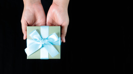 female hands holding a small gift wrapped with blue ribbon on black background