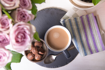 A bouquet of roses in a vase is standing with a cup of latte coffee with sweets on the windowsill of the house, top view - sweet home