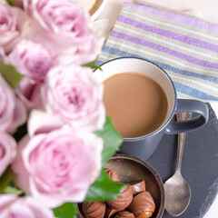 A bouquet of roses in a vase is standing with a cup of latte coffee with sweets on the windowsill of the house, top view - sweet home