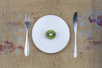 Half a stale kiwi on a white plate with a fork and a knife.