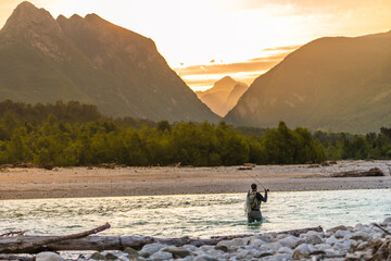 Silhouette of a fly fisherman casts his line while standing in the middle of a river, at a dawn