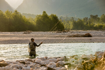 A fly fisherman casts his line while standing in the middle of a river