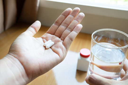 Woman's Hands Holding Pills And A Glass Of Water Before Taking Paracetamol Tablets.Medicine Plastic Bottle On Wooden Table Background. Sick And Treatment Concept.