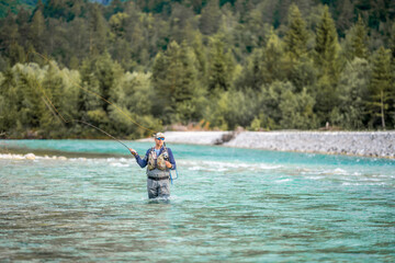 A fly fisherman casts his line while standing in the middle of a river