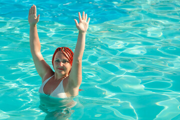 A young woman with African pigtails stands in the water in the pool with raised hands.