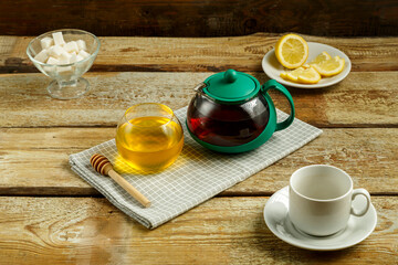 Kettle with brewed tea and honey with lemon and a cup on the table.