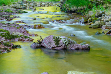 Naklejka na ściany i meble Long exposure picture of a stream flowing with rocks and natural light 