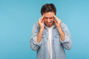 Portrait of frustrated unhealthy man in denim shirt pressing fingers to temples, feeling sick and...
