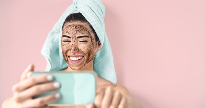 Young Smiling Woman Taking Selfie While Doing Coffee Scrub Facial Mask - Happy Girl Having Skin Care Spa Day At Home - Healthy Alternative Natural Exfoliation Treatment And Technology Concept