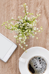 Bouquet of lilies of the valley on a table with a cup of coffee and a telephone