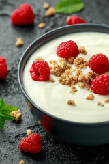 Greek yogurt with granola and raspberry in black bowl. Healthy breakfast food or snack