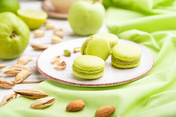 Green macarons or macaroons cakes with cup of coffee on a white wooden background. Side view, selective focus.